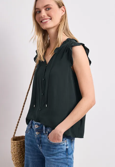 Frau trägt schwarze ärmellose Bluse, Jeans und Strohtasche.