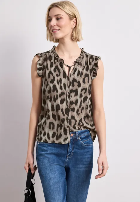 Frau in ärmelloser Bluse im Leopardenmuster, Jeans und einer kleinen schwarzen Handtasche.