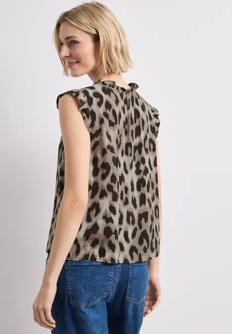 Frau mit ärmelloser Leopardenmuster-Bluse und blauen Jeans, von hinten vor weißem Hintergrund