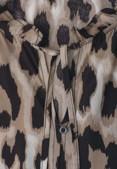 Nahaufnahme einer Bluse mit Leoprint, Knopf und Band am Ausschnitt.