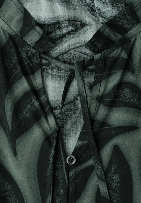 Nahaufnahme eines kapuzenartigen Kleidungsstücks mit Kordelzug und Lippen-Print in grünen und schwarzen Farbtönen.