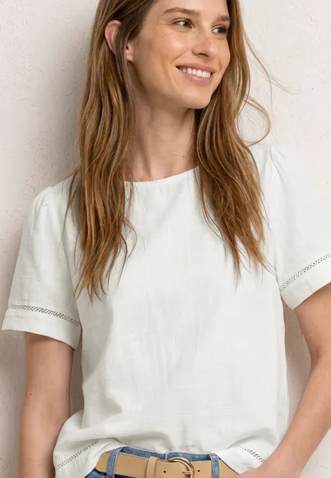 Person trägt schlichtes weißes T-Shirt und Jeans mit blauem Gürtel vor neutralem Hintergrund