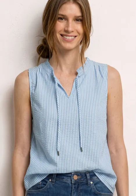 Frau in ärmelloser, blau-weiß gestreifter Bluse vor neutralem Hintergrund.