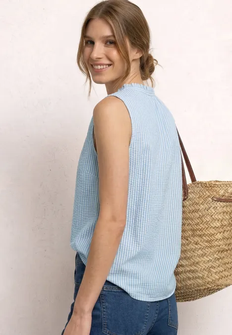 Seitliche Ansicht einer Frau in hellblauem Top und Jeans, mit geflochtener Strohtasche über der Schulter.