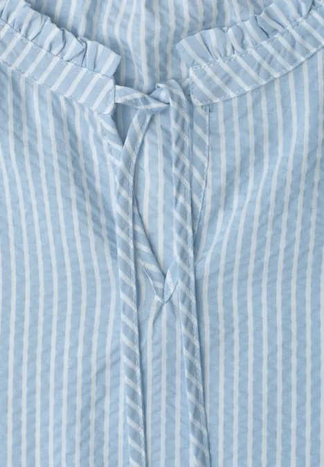 Hellblaue Bluse mit weißen Streifen und Bindeband am gerüschten Ausschnitt.
