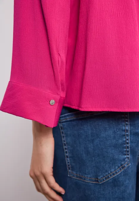 Detail eines pinken Hemdsärmels mit Manschette und einer Hand über einer Jeanshosentasche.