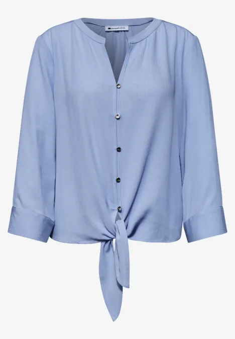 Lichtblauwe blouse met knoopsluiting, driekwartmouwen en voorstrik.