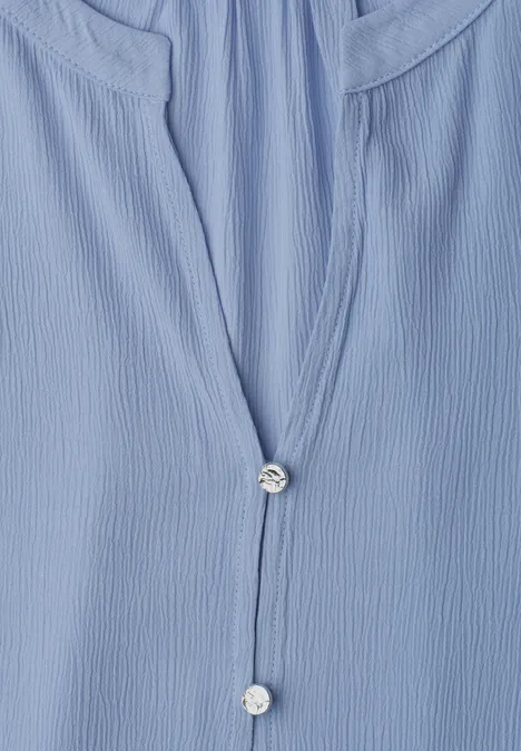 Close-up van een lichtblauw, geplooid shirt met kleine parelmoeren knopen.