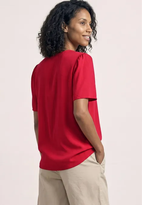 Person vue de dos portant un t-shirt rouge et un pantalon beige, mains dans les poches