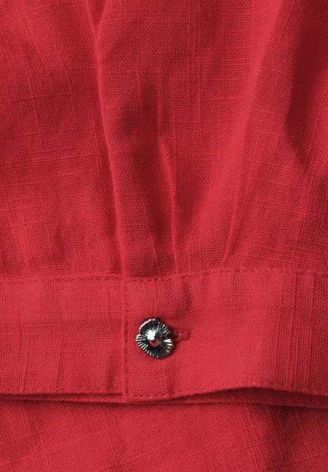 Rotes Stoffstück mit schwarzem Knopf an einer Saumkante.