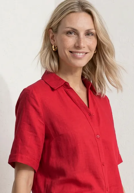 Eine blonde Frau mit verschwommenem Gesicht trägt ein rotes Kurzarmhemd vor weißem Hintergrund.