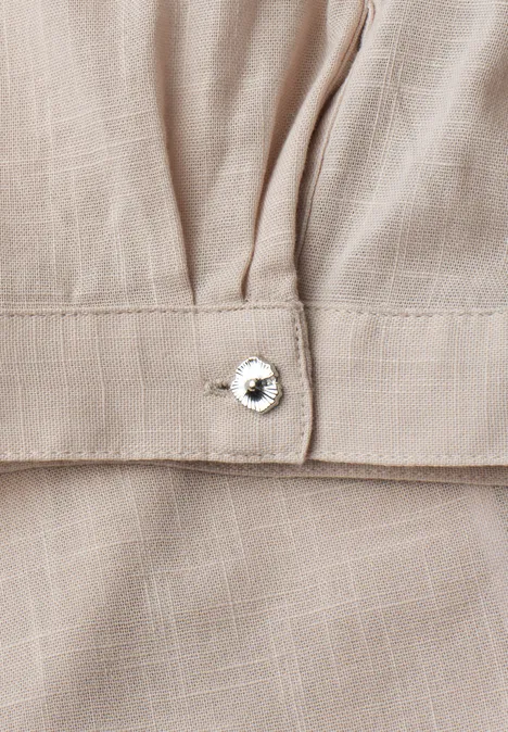 Detail eines beigen Leinenkleides mit Zierlasche und funkelndem Strassknopf.