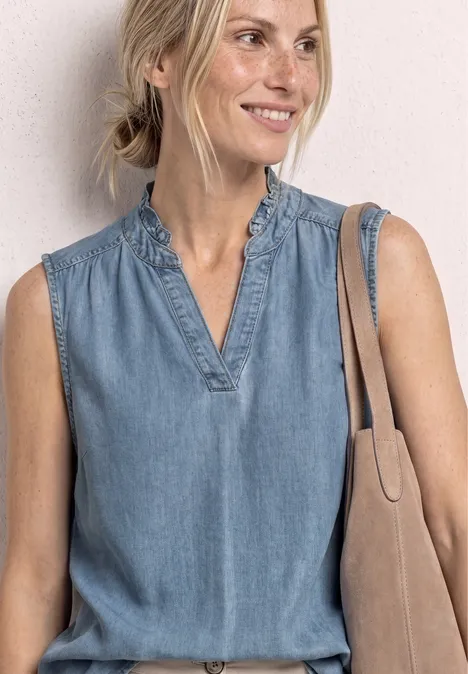 Oberkörper einer Frau in ärmelloser Jeansbluse mit V-Ausschnitt und Schultertasche