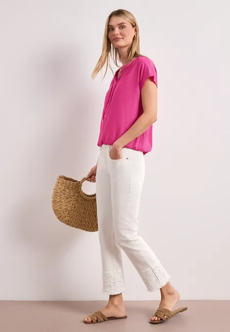Vrouw in roze blouse en witte korte broek met sandalen, draagt een gevlochten tas.
