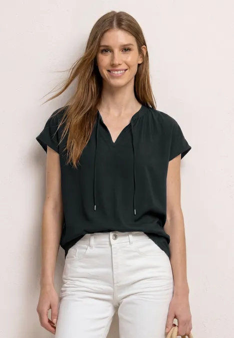 Vrouw in zwarte blouse en lichte high waist jeans voor neutrale achtergrond.