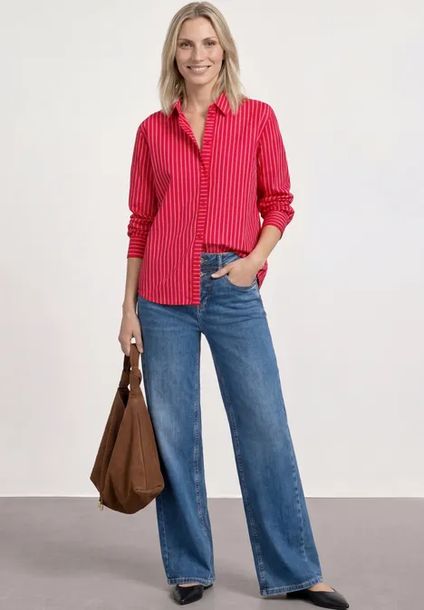 Vrouw draagt rode gestreepte blouse los in wijde blauwe jeans, met een bruine handtas.