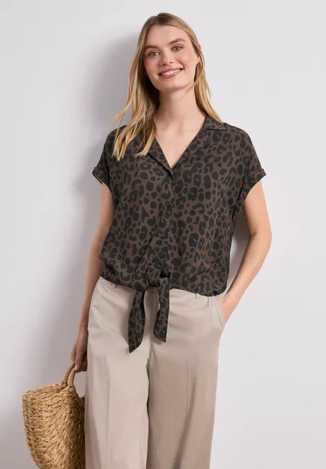 Femme en chemise léopard nouée, pantalon large beige et sac en osier