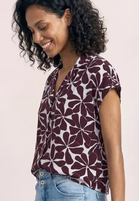 Eine Person von der Seite trägt eine bordeauxrote Bluse mit großen weißen Blumenprints.