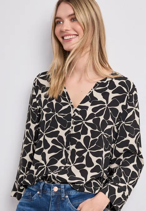 Frau in schwarz-weißer, blumenbedruckter Bluse und blauer Jeans, Gesicht unscharf.