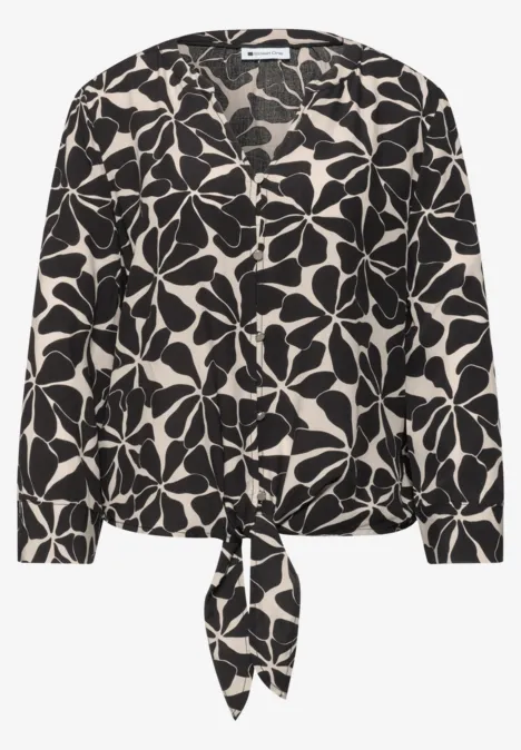 Schwarz-weiße Bluse mit großem Blumenmuster und Knoten am Saum.