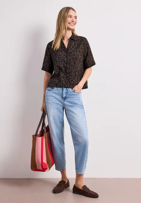 Femme en chemisier à motifs, jean bleu clair, mocassins marron et sac coloré.
