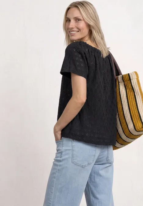 Rückansicht einer Frau in schwarzem T-Shirt, hellblauen Jeans und gestreifter Einkaufstasche.