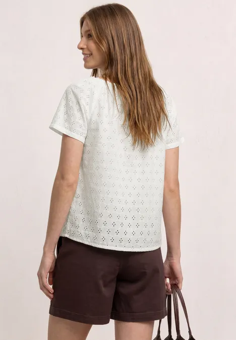 Frau von hinten in weißem T-Shirt mit Lochmuster und braunen Shorts, hält eine braune Tasche.