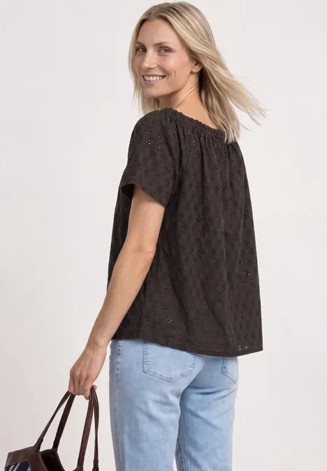 Vrouw gekleed in een zwarte blouse met structuur en lichtblauwe spijkerbroek, met een bruine tas in haar hand.