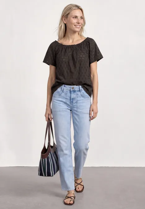 Vrouw in zwart t-shirt, lichtblauwe jeans, sandalen en een gestreepte tas.