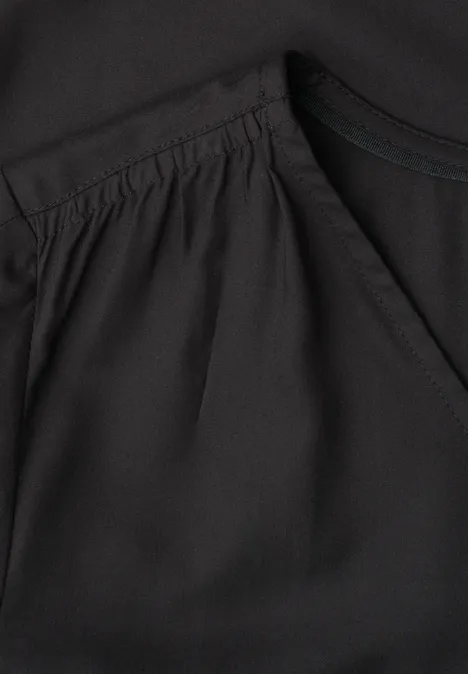 Detailaufnahme eines schwarzen Oberteils mit Falten und Eingrifftasche am Vorderteil.