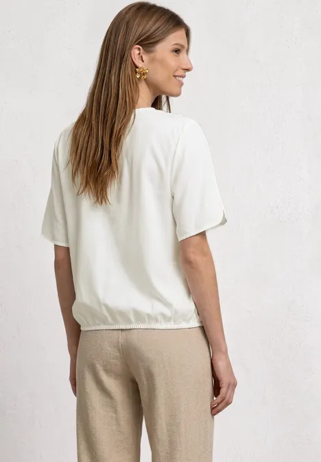 Frau von hinten in weißem T-Shirt und beigen Hosen, helle Wand im Hintergrund.