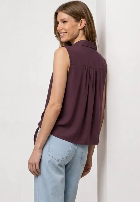 Une femme vue de dos portant un haut sans manches violet et un jean clair sur fond blanc.