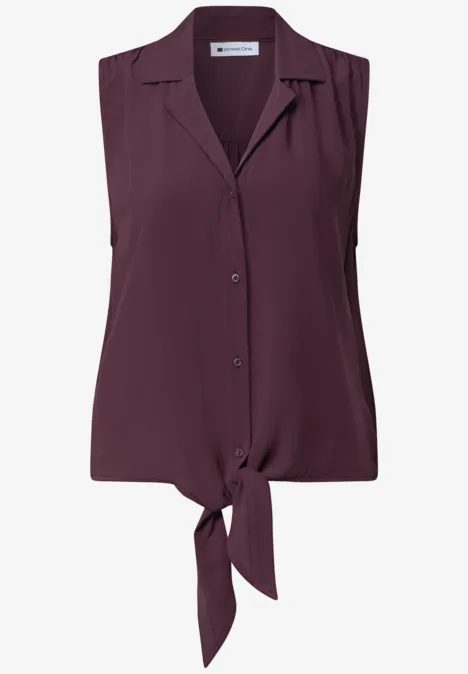 Blouse sans manches couleur prune avec boutons et nœud à l’avant.