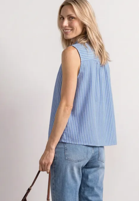 Eine Frau von hinten in blau-weiß gestreiftem ärmellosem Top mit Ringen am Schulterbereich und Jeans.