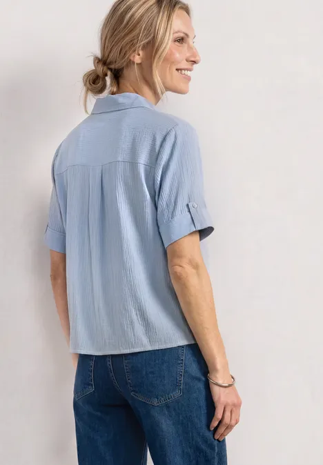 Kurzarm Hemdbluse mit Turn-Up-Details cashmere blue Frau von hinten in hellblauem Hemd und Jeans, Haar zu Dutt gebunden, lockere, lässige Pose.