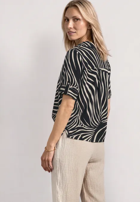 Kurzarm Hemdbluse mit Turn-Up-Details Black Frau steht seitlich, trägt ein schwarz-weiß gestreiftes Oberteil und helle, weite Hose