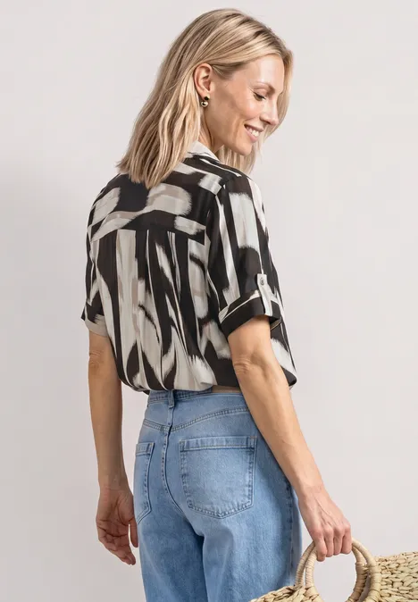 Kurzarm Hemdbluse mit Turn-Up-Details espresso brown Frau mit Zebramuster-Bluse, hellen Jeans und Strohtasche, Blick abgewandt.