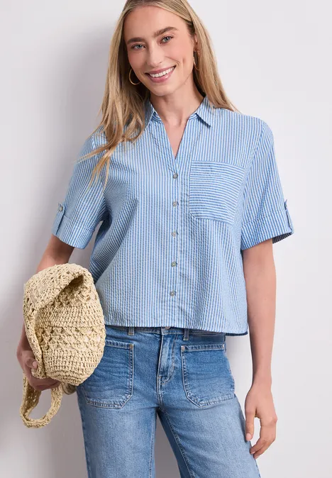 Vrouw in lichtblauw hemd met korte mouwen en jeans, houdt een strohoed vast.