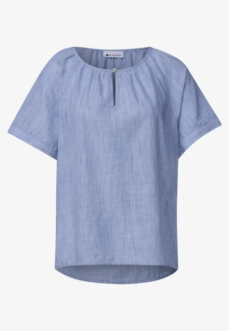 Hellblaue, locker fallende Bluse mit kurzen Ärmeln, kleinem Schlitz am Rundhalsausschnitt und dezenter Struktur.