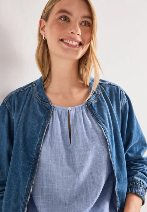 Person trägt offene Jeansjacke über hellblauer Bluse, Ausschnitt bis Brusthöhe.