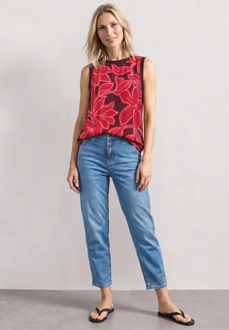 Blusentop mit Rundhals und Tape-Detail salsa red Frau in rotem, floralen Top, blauen Jeans und schwarzen Sandalen vor neutraler Wand.