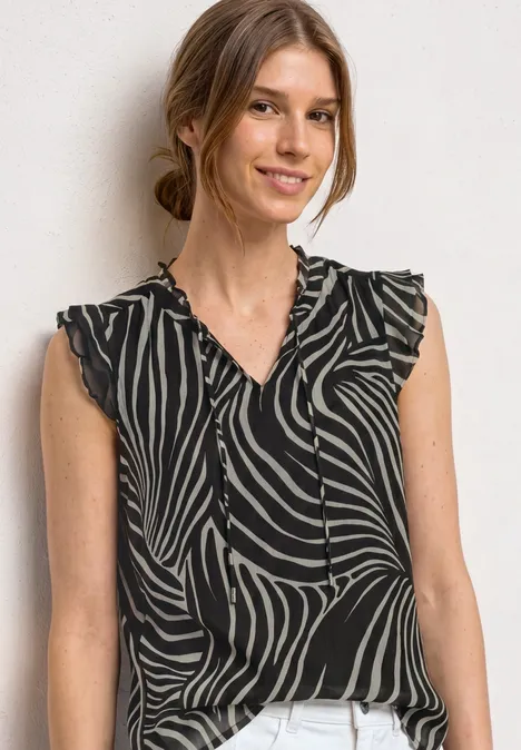 Frau in ärmelloser, schwarz-weißer Zebra-Bluse mit V-Ausschnitt vor hellem Hintergrund.