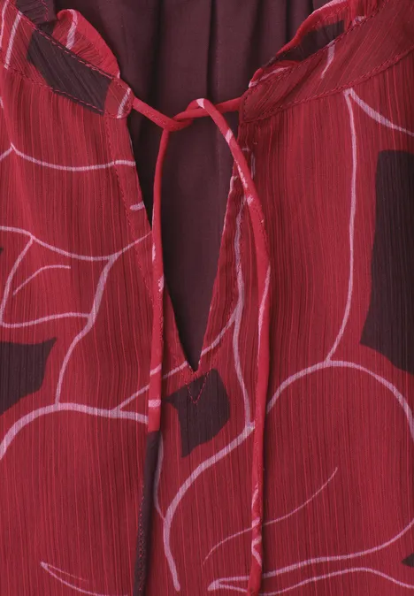 Rotes Kleidungsstück mit zartem rosa Blumenprint und kleinem Schlüsselloch-Ausschnitt mit Bindeband.