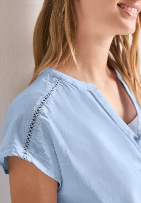 Frau trägt hellblaue Bluse mit Spitzenbesatz an der Schulter und kurzem Ärmel