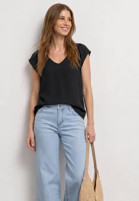 Frau trägt schwarzes V-Shirt, hellblaue Jeans und hält eine Strohtasche.