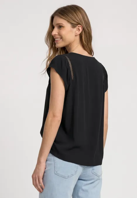 Frau steht mit dem Rücken zur Kamera, trägt schwarzes T-Shirt und helle Jeans.