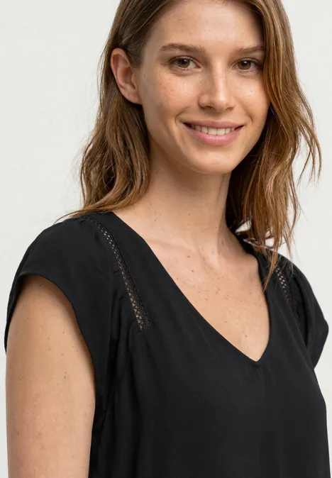 Eine Frau mit langen Haaren trägt ein schwarzes V-Ausschnitt-Oberteil.