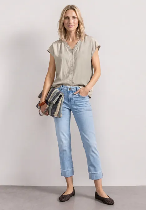 Vrouw met beige top, opgerolde spijkerbroek, bruine ballerina’s en gestreepte schoudertas.