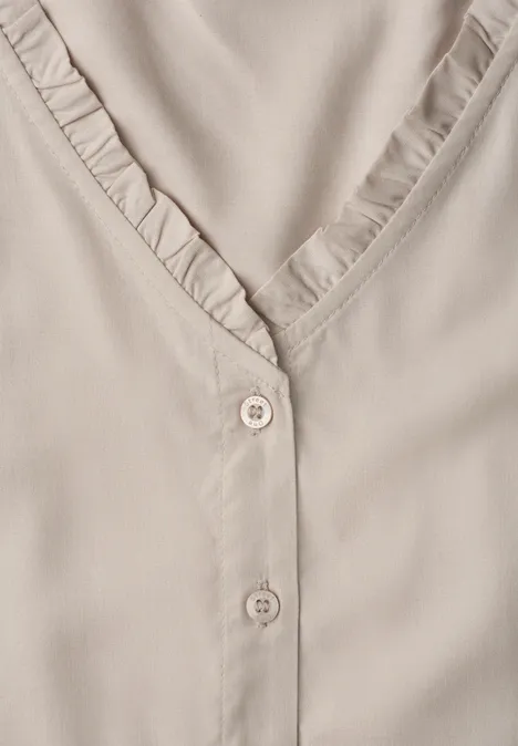 Beige blouse met V-hals, ruches langs de kraag en twee subtiele knoopjes.