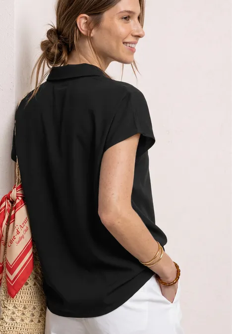 Chemisier à col chemise et ourlet élastiqué Black Femme de profil, t-shirt noir, pantalon blanc, sac en osier avec foulard rouge.